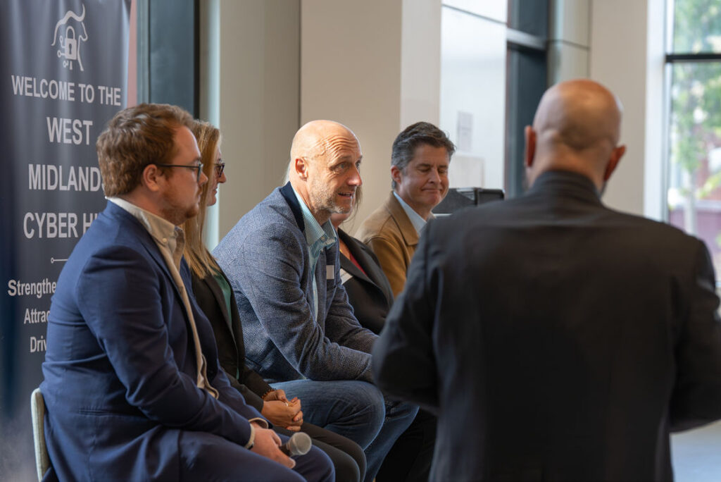 Attendees talking beside the West Midlands Cyber Hub welcome banner
