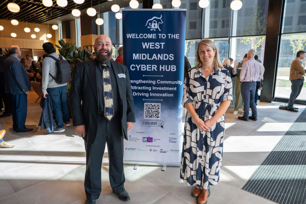Two people beside the West Midlands Cyber Hub welcome banner